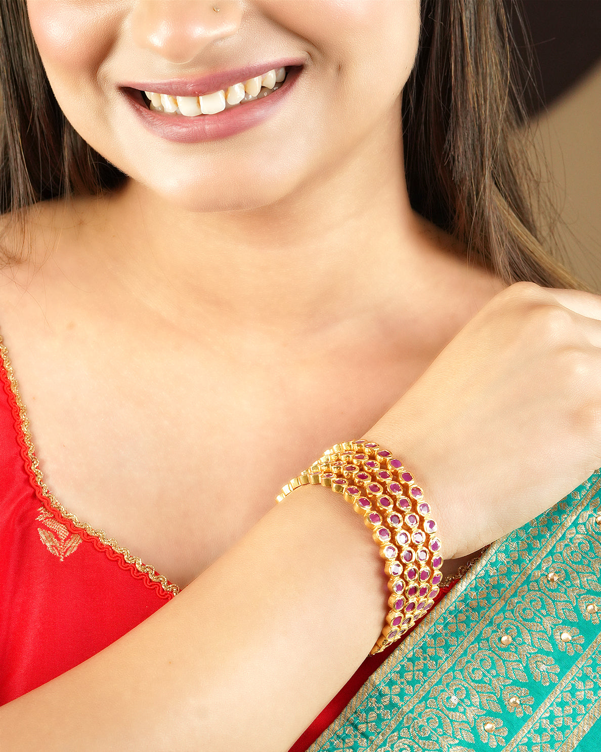 A woman wearing a gold bracelet with pink gemstones on her wrist.