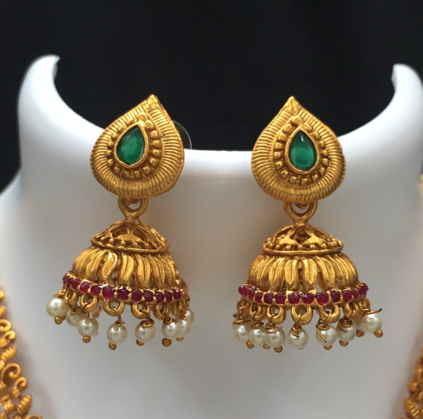 Gold jhumka earrings with green stones, red accents, and pearl danglers.
