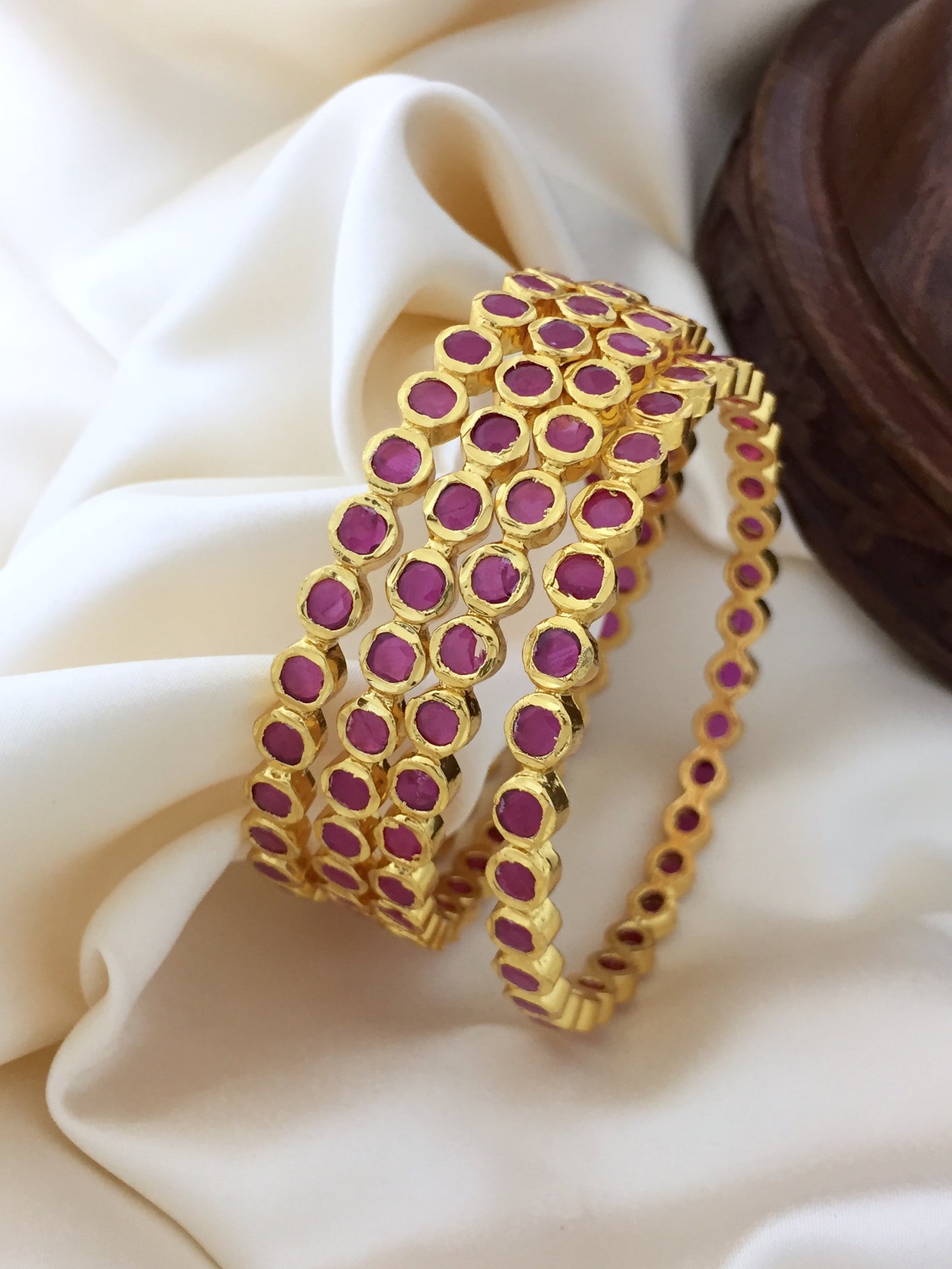 Two gold bangles adorned with small, round, pink gemstones.