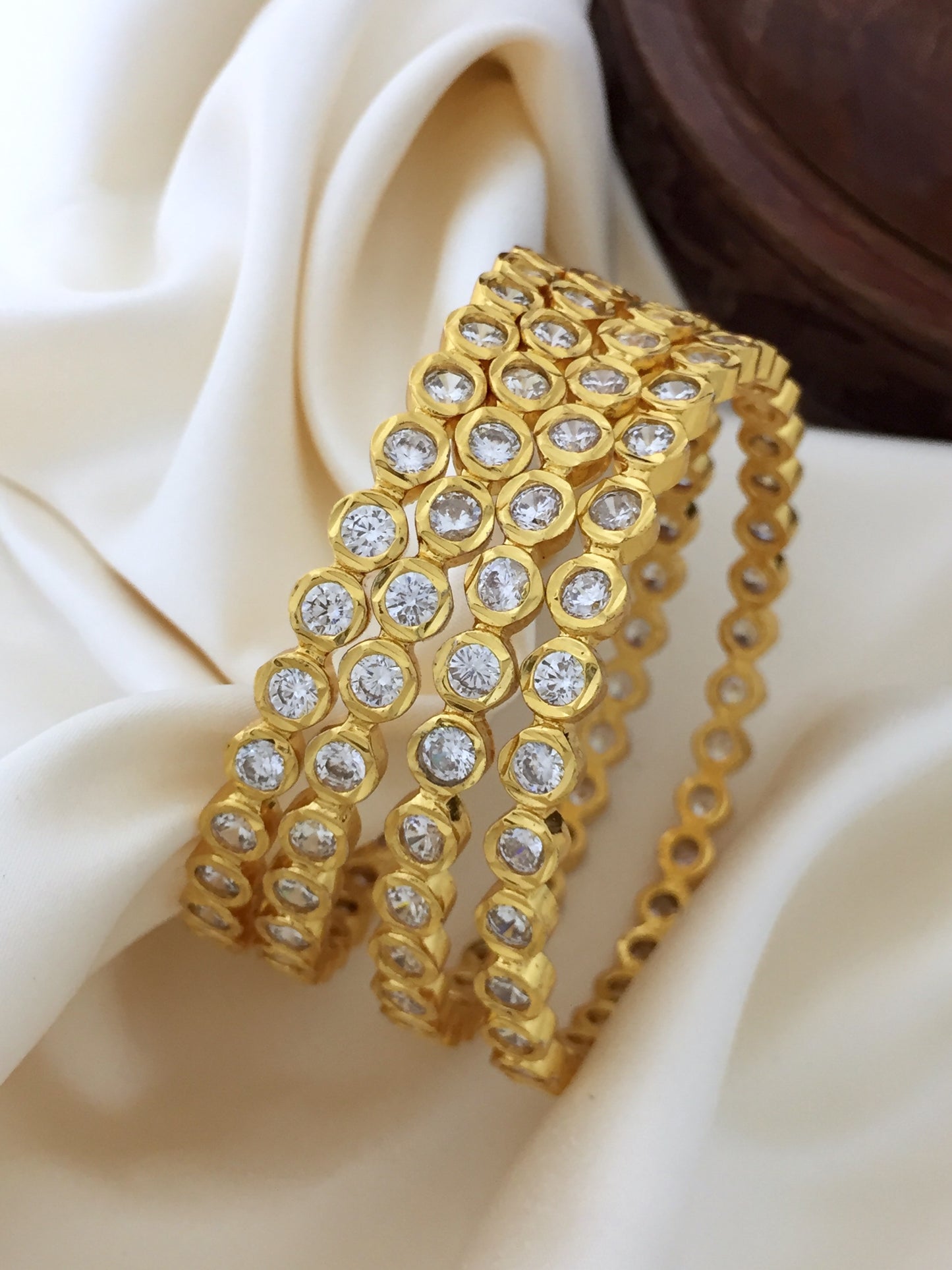 Three gold bangles adorned with circular diamond-like stones.