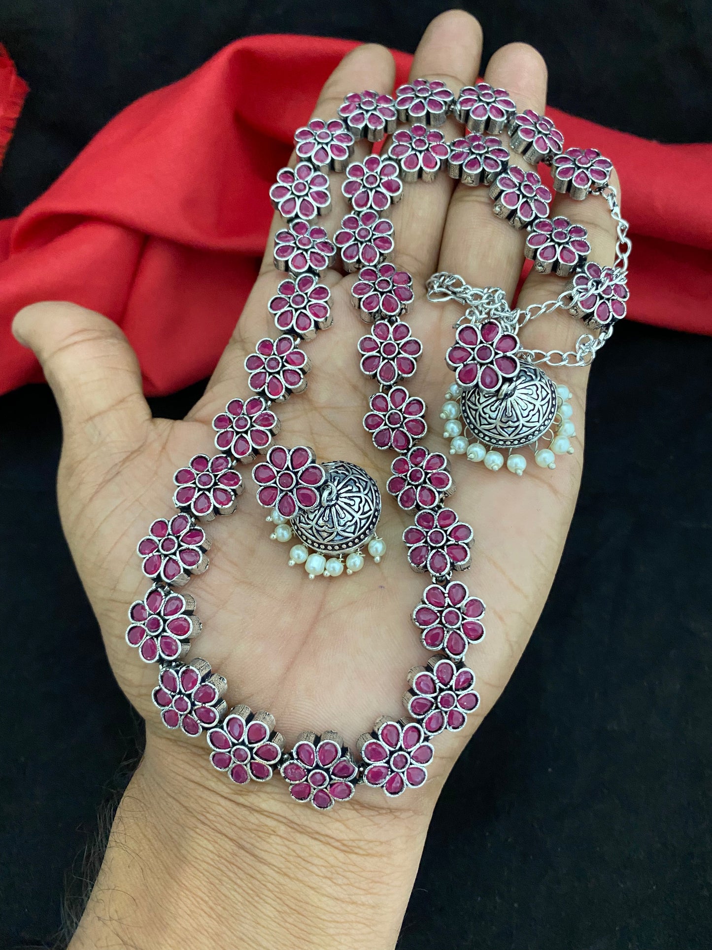 Silver floral necklace and earrings set with pink accents held in a hand.