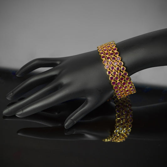 A gold bracelet with multiple red gemstones displayed on a black mannequin hand.