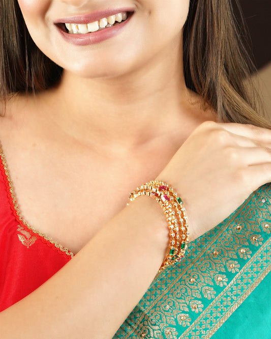 A woman wearing a red and green traditional outfit, showcasing a set of gold and multicolored beaded bangles on her wrist.