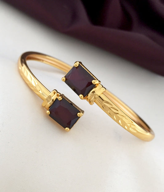 A gold bracelet with two rectangular garnet stones.