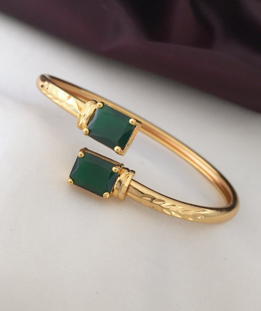 A gold bracelet with two rectangular green gemstones.