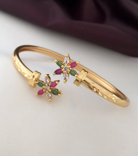 Gold bangle with floral gemstone design featuring red, green, and clear stones.