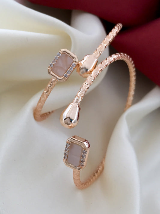 Rose gold twisted bangle with two square gemstone accents and small diamond details.