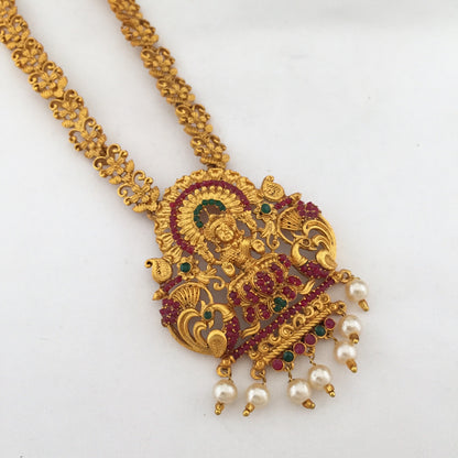 Gold necklace with an intricate pendant featuring a deity, adorned with red and green gemstones and pearl drops.