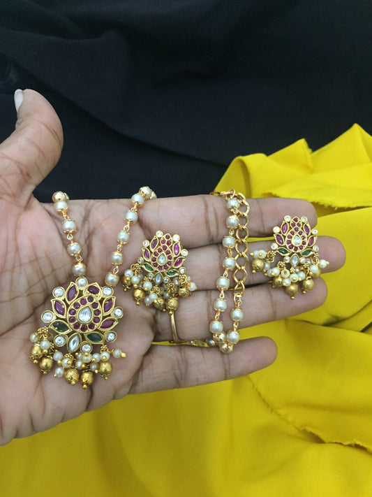 A hand holding a set of traditional jewelry, including a necklace and matching earrings, adorned with pearls, gold beads, and intricate floral designs.