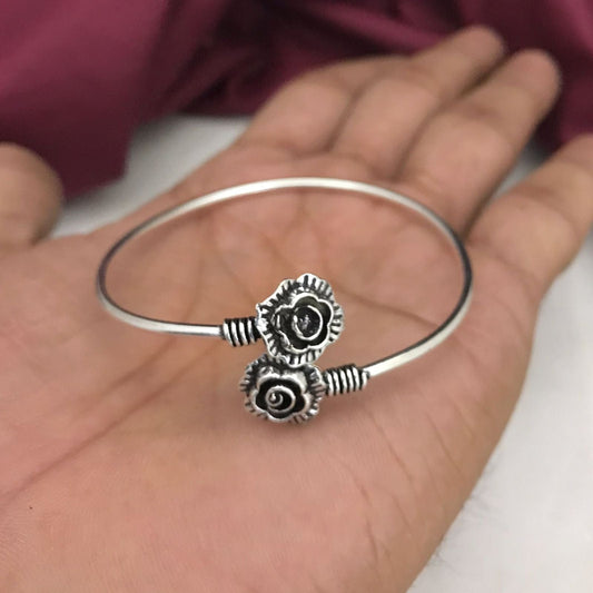 Silver bangle bracelet with two rose-shaped charms.