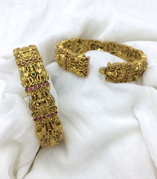 Two intricately designed gold bracelets adorned with red and green gemstones.