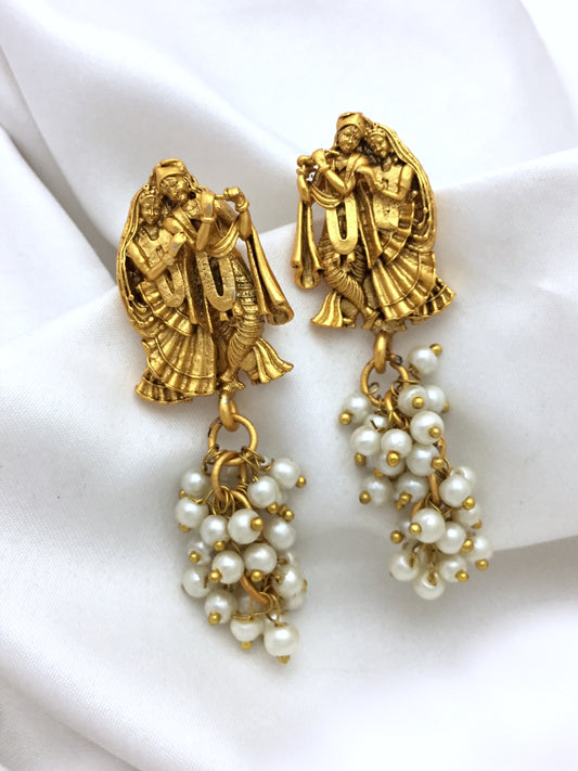 Gold earrings featuring intricate designs of two figures playing musical instruments, with clusters of small white pearls hanging below.