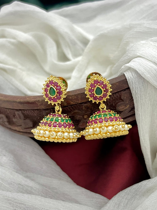 A pair of gold jhumka earrings adorned with red and green gemstones and pearl detailing.