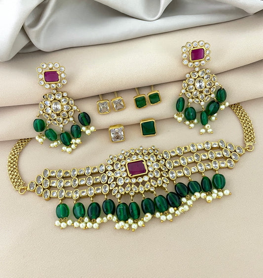 A gold jewelry set featuring a choker necklace with green and white stones, matching earrings, and additional stud earrings.