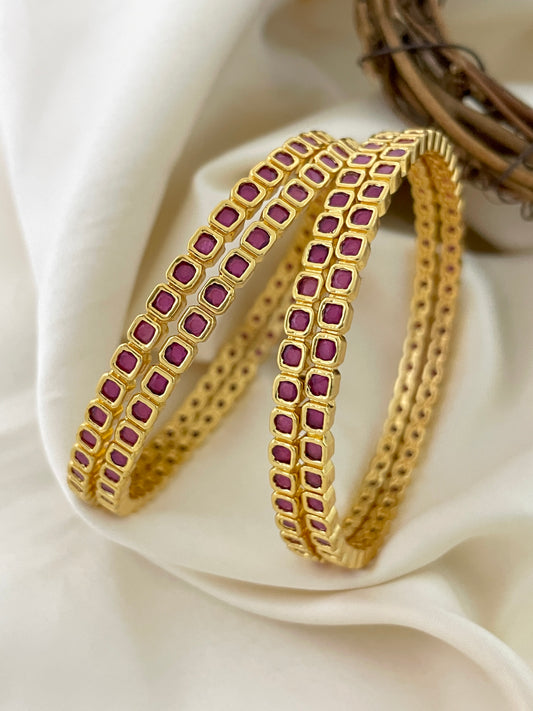 Two gold bangles adorned with small square red gemstones.
