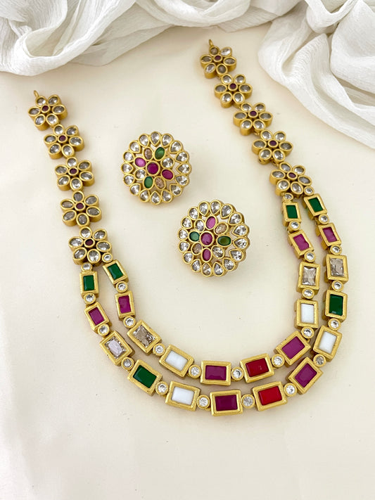 A gold necklace set with matching earrings, featuring multicolored gemstones in red, green, white, and pink.