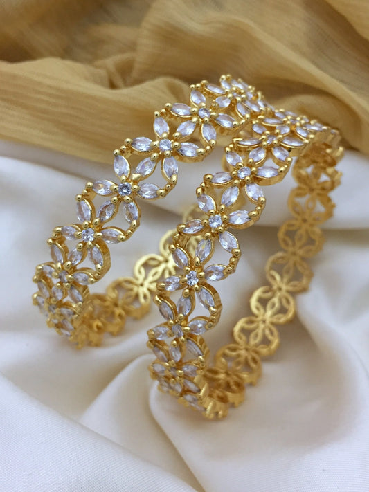Two gold bangles with intricate flower designs adorned with American diamonds.