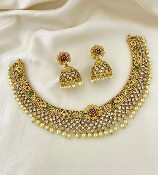 A gold-plated choker necklace with intricate designs, adorned with pearls and gemstones, accompanied by matching earrings.